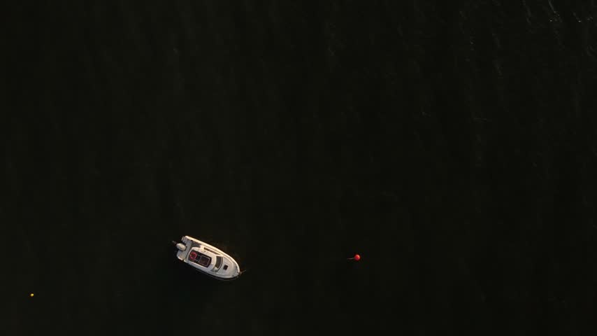 Minimalist aerial perspective of a solitary motor boat floating on ripples of emerald coastal water.