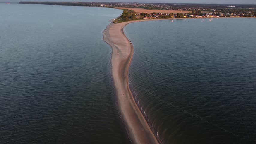 Drone shot of a scenic sunset over the bay, showing a thin sandy spit surrounded by deep dark waters.