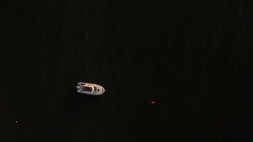 Minimalist aerial perspective of a solitary motor boat floating on ripples of emerald coastal water.