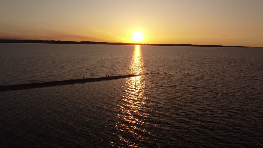Drone shot of a scenic sunset over the bay, showing a thin sandy spit surrounded by deep dark waters.