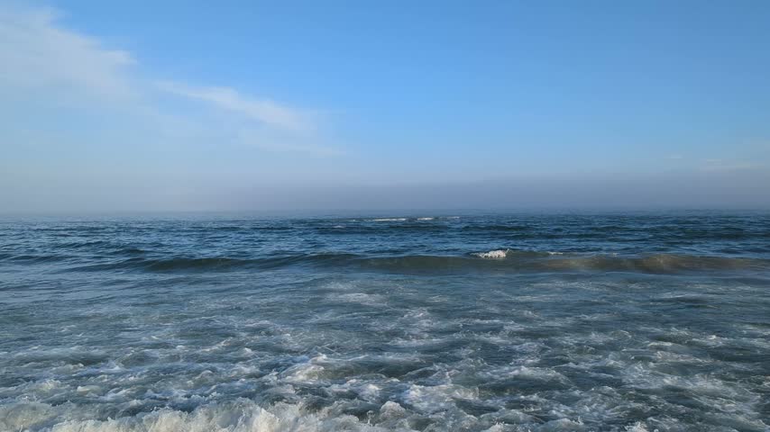 Bright morning at sea, blue waves breaking into white foam while droplets scatter in clear light