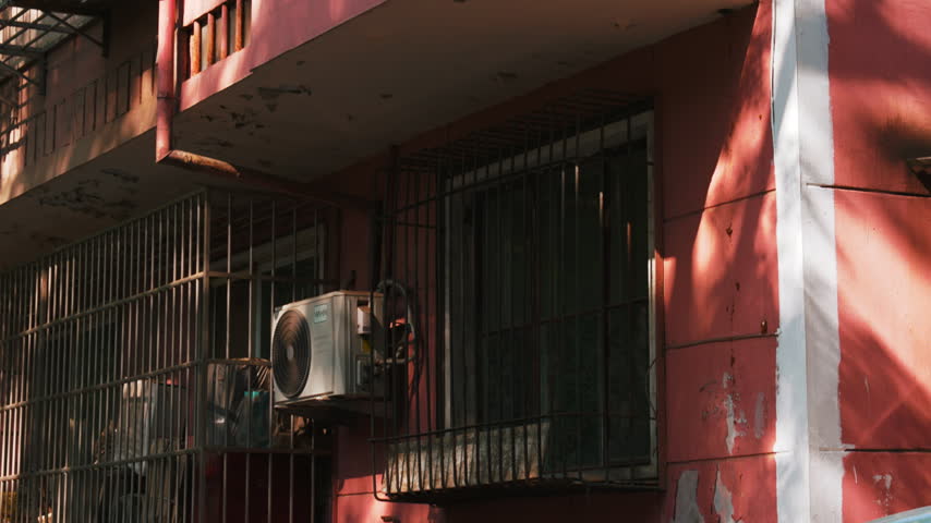 A low-angle shot tilts upward to reveal a glass-enclosed balcony and weathered pink facade on an old apartment building in Xuanwumen, Beijing, China.