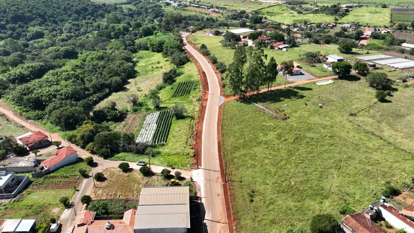 Aerial flight above a paved country road beside crop rows and green pasture near Cambui, Minas Gerais, Brazil.