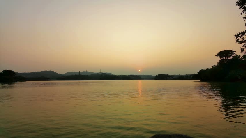 Serene sunset over calm lake with distant hills and golden evening sky