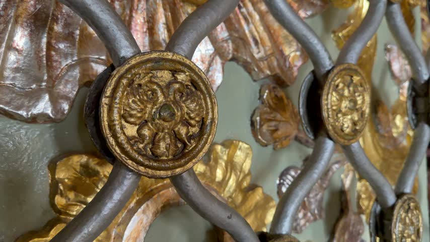 Close up of an antique decorative metal lattice with golden floral ornaments and round badges. Vintage baroque architectural detail with golden leaf elements on an old wall background.