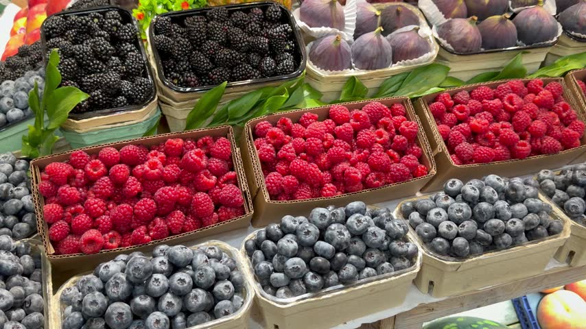 Various types of fresh berries and figs are displayed in cardboard boxes at a market stall. Healthy organic food, fresh summer harvest, delicious sweet desserts, grocery store display.