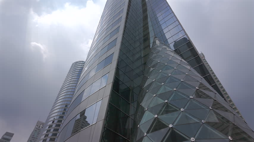 Looking around the Modern commercial architecture framed by trees and atmospheric clouds in a bustling city in Bangkok, Thailand.