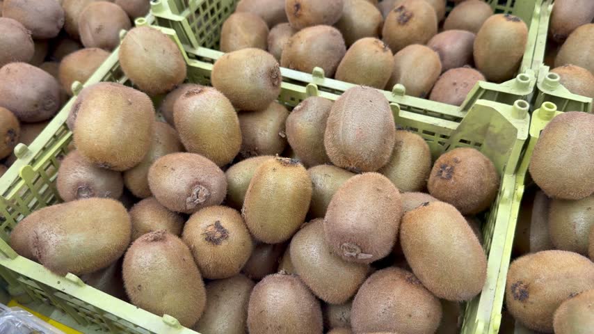 Fresh kiwi fruits fill plastic crates on display in a grocery store. Raw fruit, organic food, supermarket display, grocery shopping.