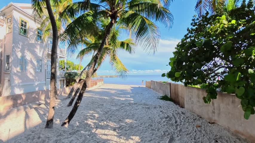 Beach approach framed by palms and buildings beside the sea in Key West Florida.