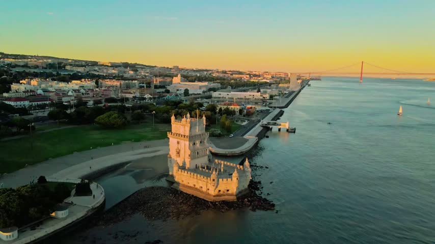Aerial view of Belém Tower in Lisbon, Portugal, at dusk, capturing the historic riverside fortress, distinctive architecture, and atmospheric evening light in real-time cinematic footage.