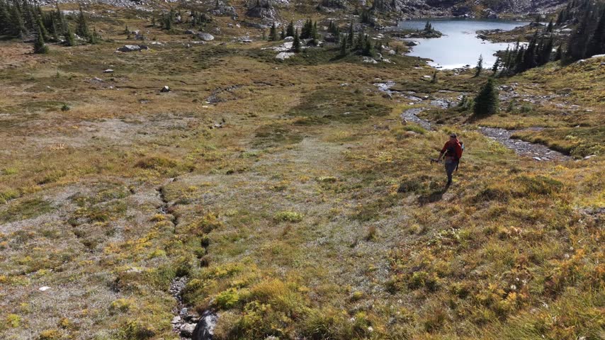 A hiker follows a narrow rocky path through alpine terrain near Sheila Lake on Trophy Mountain, Wells Gray Provincial Park, British Columbia, Canada.