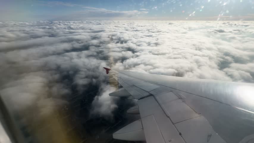 view from the window of an airplane to the wing of an airplane in clear sunny weather, flying over clouds