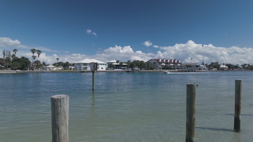 A wooden boardwalk runs beside a calm coastal canal in Treasure Island,FL as dramatic storm clouds gather overhead, with waterfront homes, docks and a small boat visible in the distance, conveying tension and anticipation.
