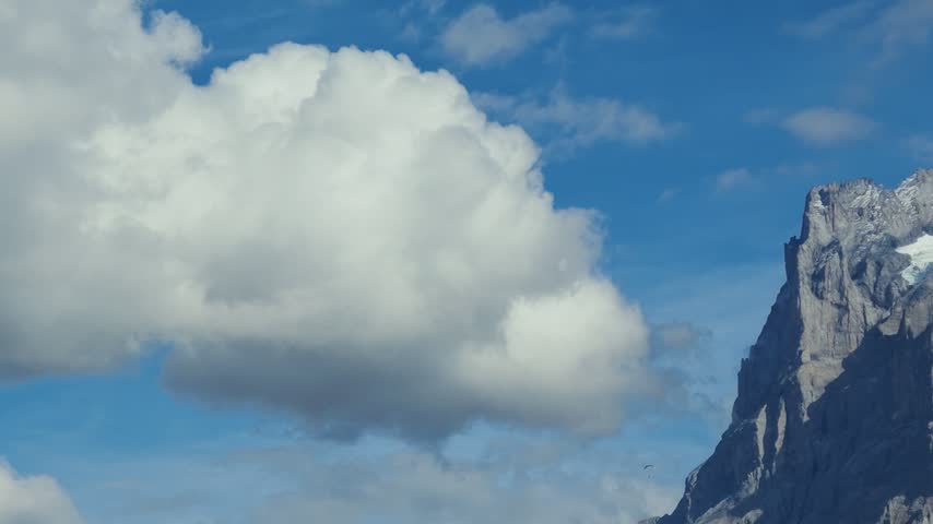 Sunlight illuminates a rugged, snow-covered mountain above Grindelwald beneath drifting clouds and a blue autumn sky.