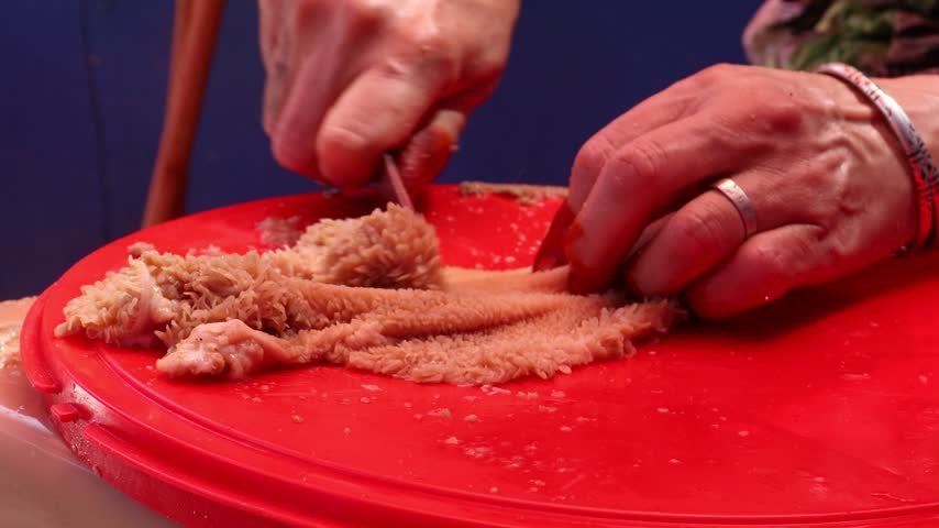 Hands cutting cleaned sheep tripe into pieces on a red board, preparing Moroccan karcha offal dish during Eid al-Adha