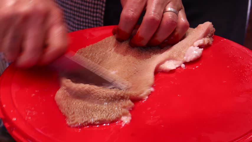 Hands cleaning raw sheep tripe with a knife on a red cutting board, traditional Moroccan karcha preparation for Eid al-Adha