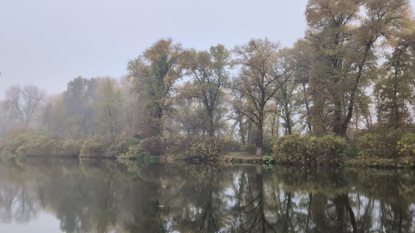 Quiet autumn river landscape with foggy trees and reflection