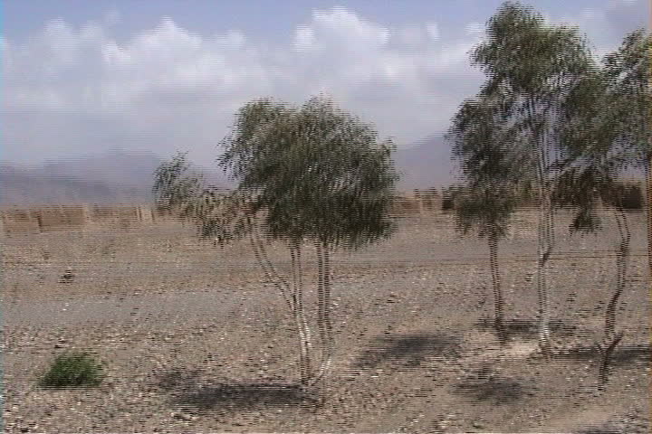 Drive through nearly barren, desolate land. Passes some scruffy trees and mud brick village in distance in South Waziristan, Pakistan.