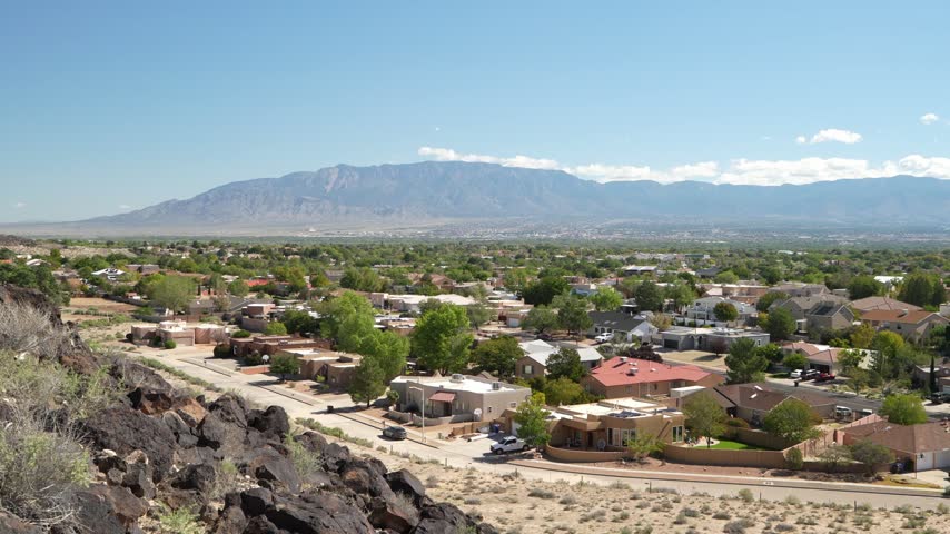 Aerial drone footage panning over a residential neighborhood in New Mexico with the Sandia Mountains in the background.