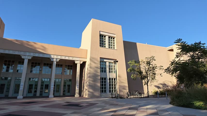 Exterior view of the Zimmerman Library building featuring adobe-style architecture and a paved plaza under a clear blue sky.