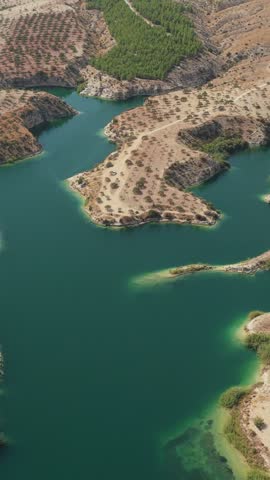 Aerial view of a winding turquoise reservoir surrounded by dry hills, planted groves, and rugged shoreline.