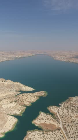 Aerial view of a broad blue reservoir bordered by arid, patterned terrain and winding access roads.
