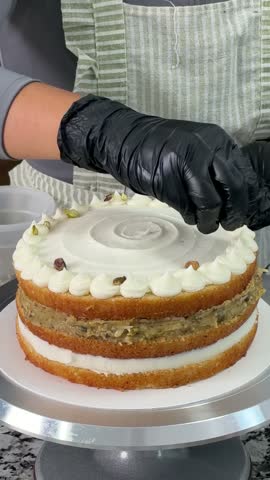 Sprinkling chopped pistachios on a vanilla buttercream naked cake