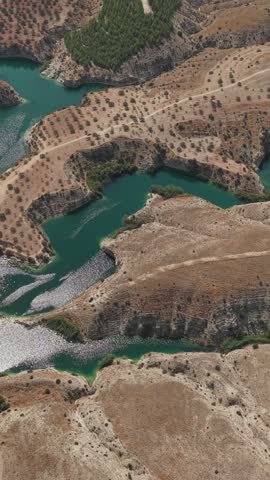 Aerial view of a winding turquoise reservoir surrounded by dry hills, orchards, and rugged rocky shorelines.