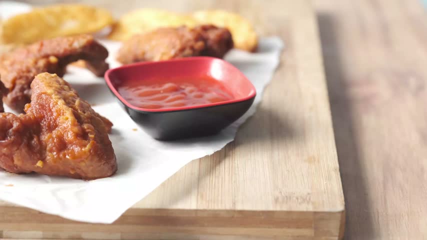 Appetizing crispy chicken wings served with potato wedges and dipping sauce on white parchment paper. Shallow depth of field video showcasing delicious hot meal details and texture.