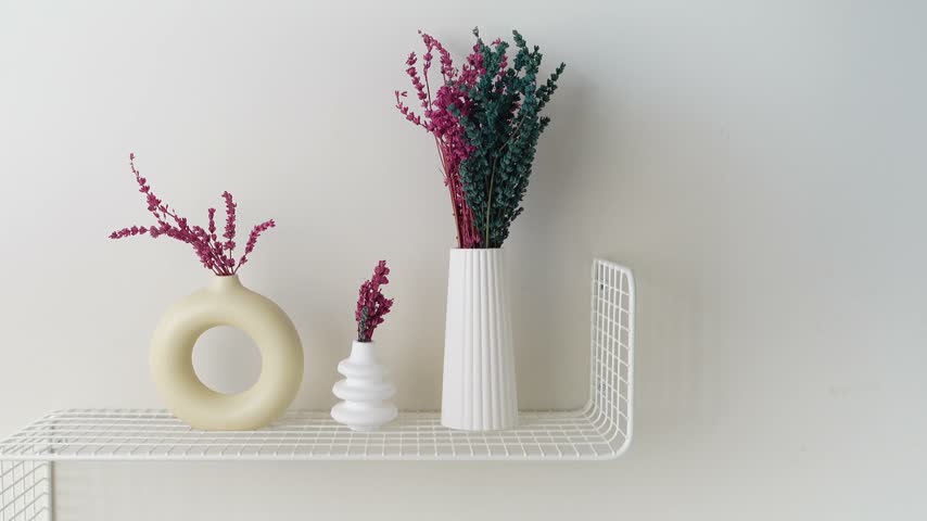 Clean modern interior shelf displaying three distinct ceramic vases holding vibrant pink and blue dried lavender flowers against a plain white wall aesthetic video clip.