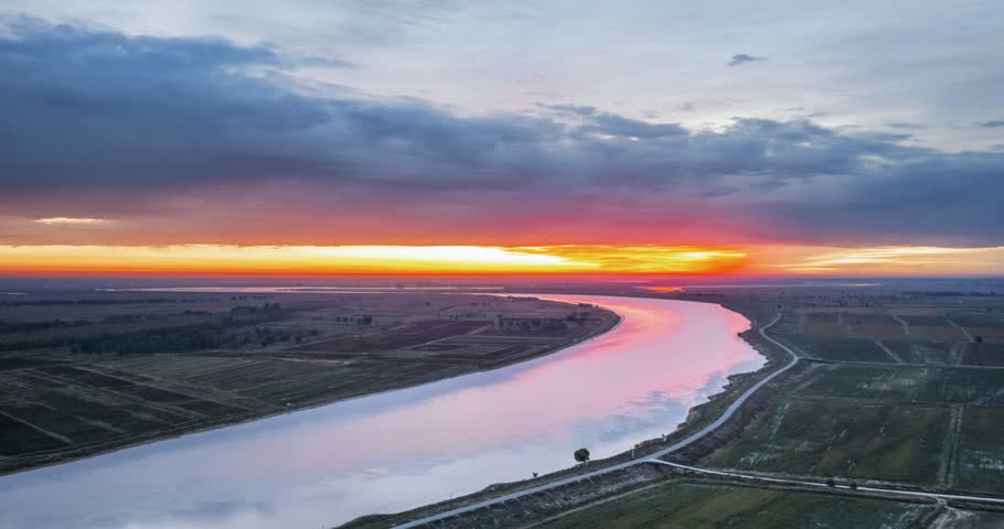 Aerial dawn time-lapse of winding Yellow River, sunrise gilding meandering channels, sorghum fields and loess banks, Baotou city, Inner Mongolia, China.