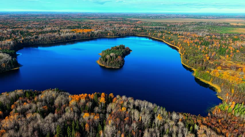 Aerial view of vibrant blue lake surrounded by autumn foliage and island of trees