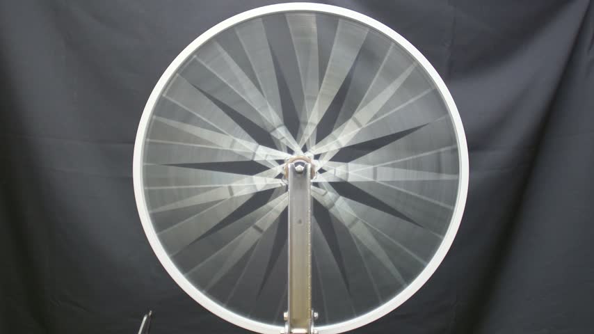Front view of a freshly built bicycle wheel spinning in a truing stand against a black cloth, spokes blurring then slowing to a stop. Minimal and graphic, real time 4K.