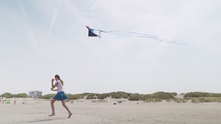 Girl running barefoot with a kite on a sandy beach sand dunes with grass in the background