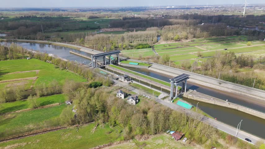 landscape twin chamber canal lock steel gates spanning waterway surrounded by green fields leafless woodland roadway scattered rural houses distant reveals long elevated wide aerial