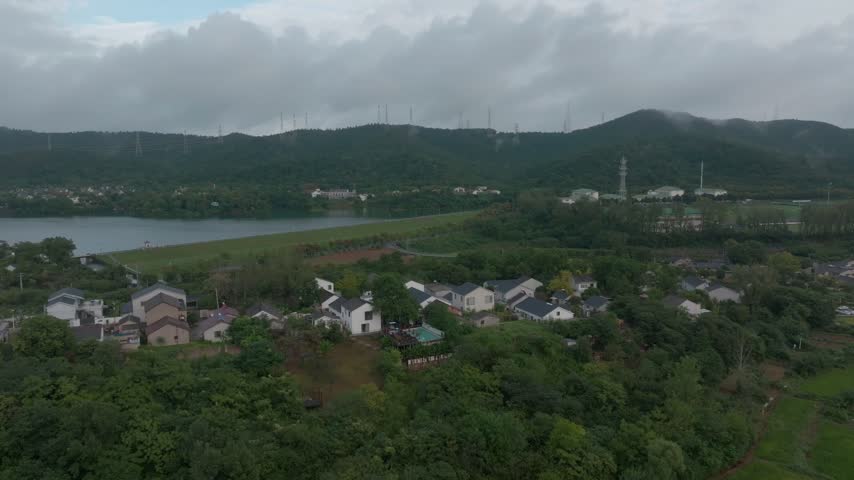Aerial view of rural houses and fields beside wooded hills.