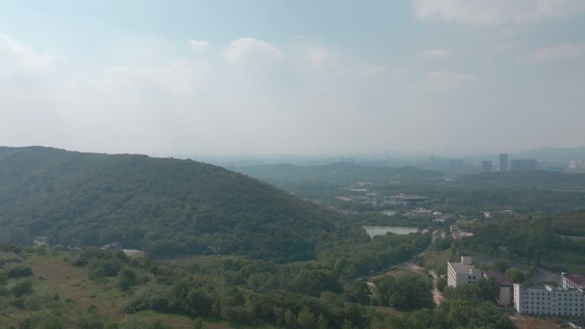 Aerial view of forested hills with the distant Nanjing city skyline in Jiangsu province China on a hazy day.