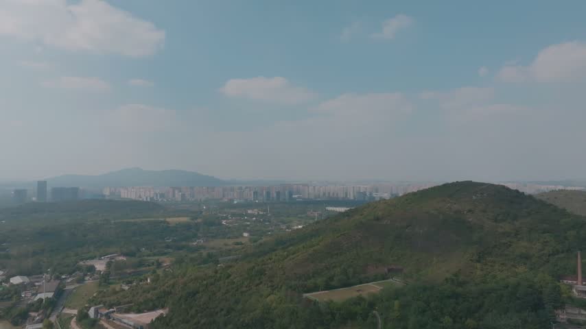 Wide aerial view of the Nanjing skyline beyond wooded hills with distant urban buildings under a hazy sky in Jiangsu China.