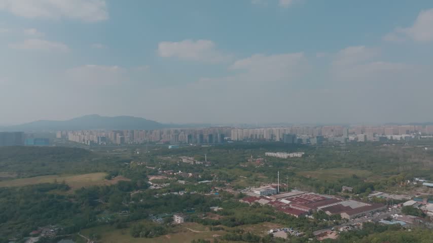 Aerial panorama of Nanjing urban development beyond forest and fields with distant city buildings in Jiangsu China.