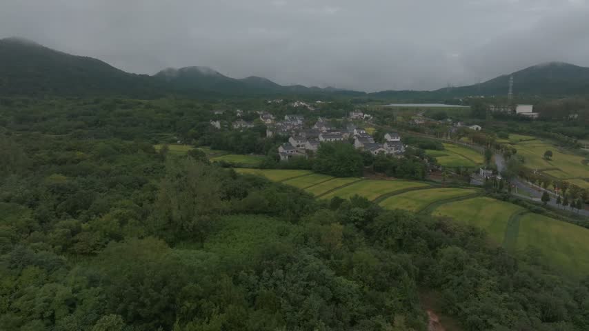 Aerial view of farmland and village houses beneath misty hills.