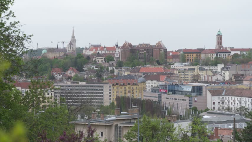 Budapest skyline with the Buda Castle District and Matthias Church above hillside buildings and rooftops.