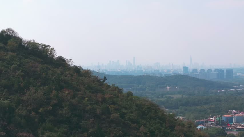 Distant Nanjing city skyline above wooded hills and nearby residential houses on a hazy day in Jiangsu province China.