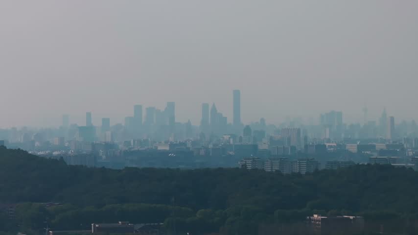 View of distant Nanjing city towers across wooded hills in hazy daylight in Jiangsu province China.