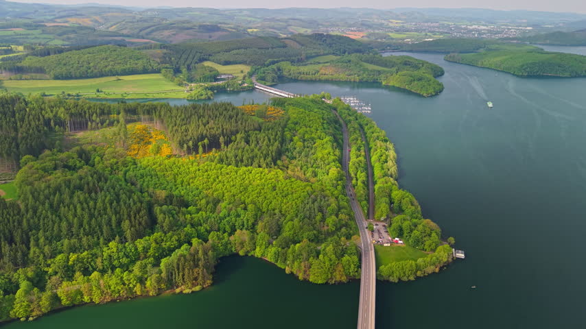 From above, Biggesee Reservoir borders a forested shoreline crossed by a long bridge near Olpe, Germany.