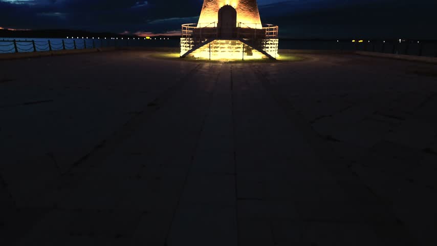 panoramic view of a vintage lighthouse illuminated on the lake shore in the blue twilight.