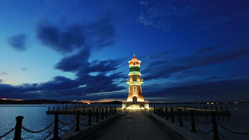 panoramic view of a vintage lighthouse illuminated on the lake shore in the blue twilight.