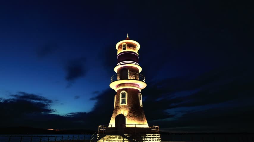 panoramic view of a vintage lighthouse illuminated on the lake shore in the blue twilight.