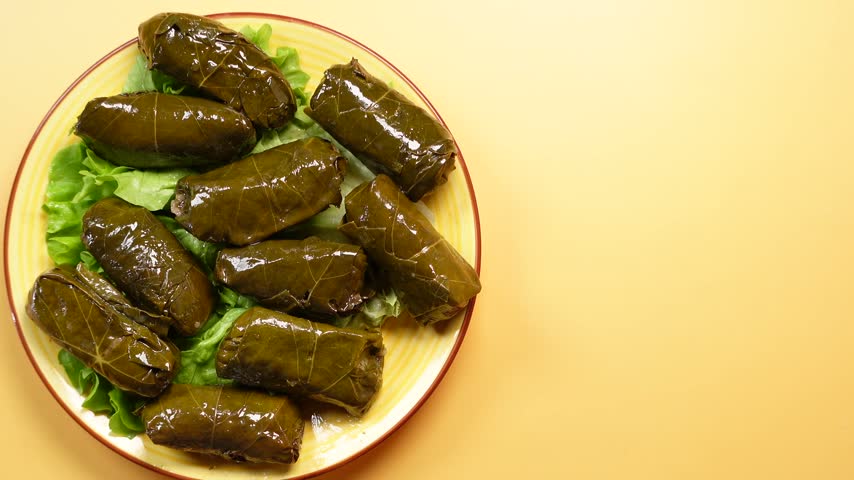 Top view of traditional dolma stuffed grape leaves arranged on a colorful plate with lettuce leaves against a warm beige background. Close up food footage.