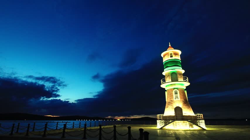 panoramic view of a vintage lighthouse illuminated on the lake shore in the blue twilight.