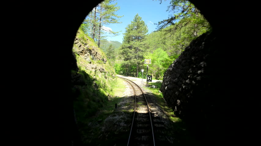 Railway Tracks Curve Toward Bright Tunnel Exit. The camera moves backward through a dark passage as daylight fades ahead